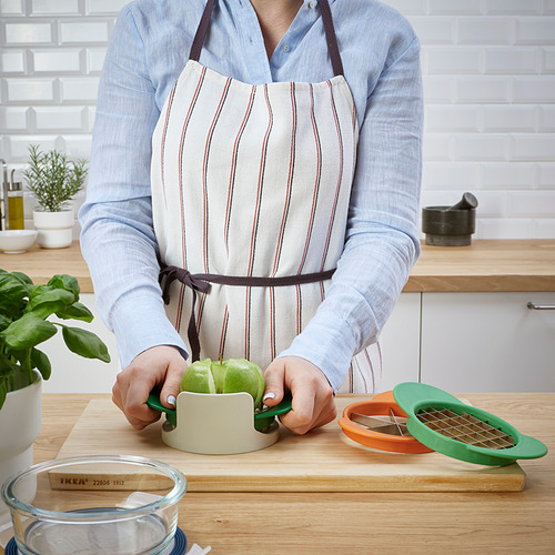 La persona que lleva un delantal usa un cortador de frutas verdes para cortar una manzana en una tabla de cortar de madera.