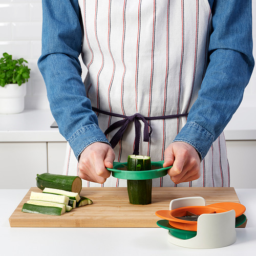 La persona prepara calabacín usando un colorido artilugio de cocina, que corta frutas y verduras de manera eficiente.