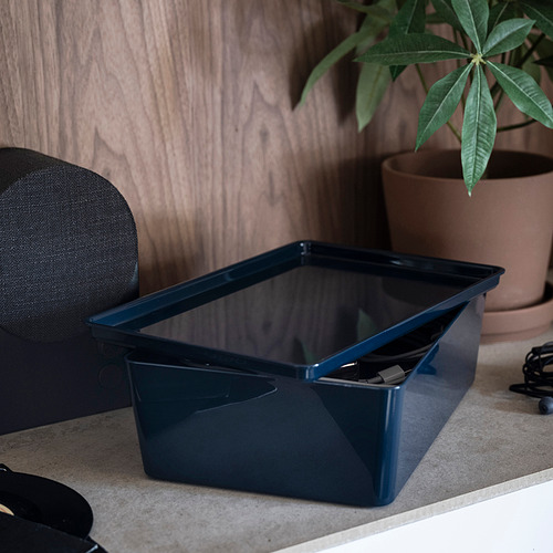 Una caja azul de KUGGIS reposa sobre un escritorio, guardando los objetos ordenadamente. La caja, con su acabado brillante, es ideal para organizar accesorios de escritorio o gadgets multimedia.