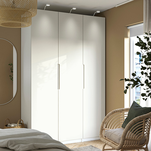 Dormitorio moderno con armario alto PAX, espejo redondo, silla de mimbre y gran ventanal.