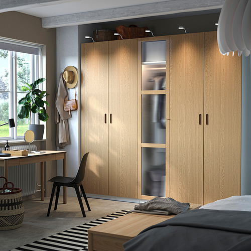 Dormitorio moderno con gran armario PAX de madera clara, silla de oficina negra, alfombra a rayas y marco de cama negro.