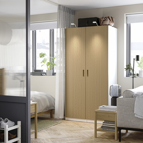 Dormitorio moderno con armario de roble TONSTAD, bisagras de cierre suave, cerca de un sillón acogedor y plantas.