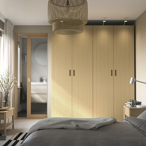 Dormitorio moderno con armario PAX, cama, mesa auxiliar y puerta de baño de cristal.