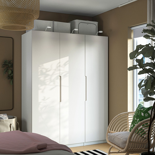 Armario PAX blanco con elegantes manijas y almacenamiento, cerca de la ventana y la silla en una habitación acogedora.