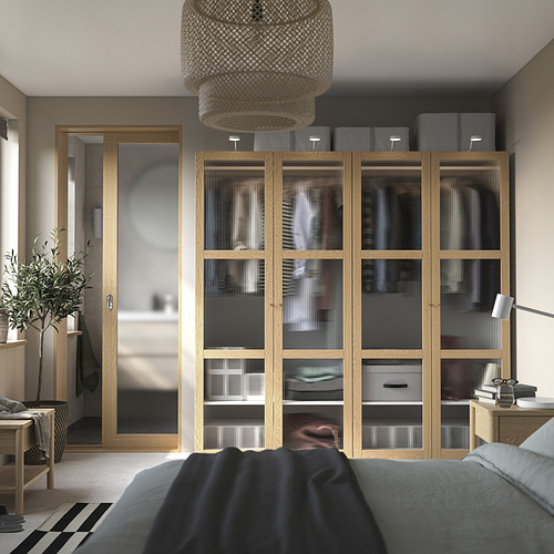 Amplio dormitorio con armario de madera, puertas de cristal, espejo, cama, mesita de noche, lámpara, planta y lámpara de mimbre.