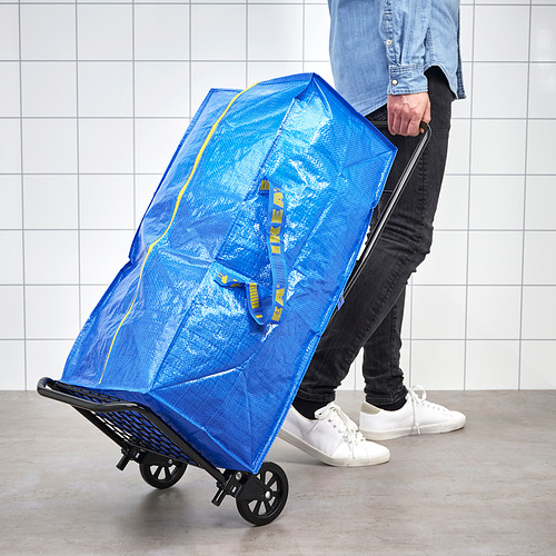 Persona empujando el carrito de compras azul FRAKTA. La bolsa es grande, fuerte y está equipada con ruedas para facilitar el transporte.