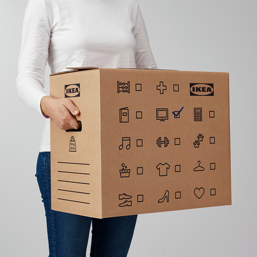 Persona sosteniendo una robusta caja de cartón de Ikea con asas recortadas para facilitar su transporte. La caja tiene símbolos y líneas para marcar el contenido.