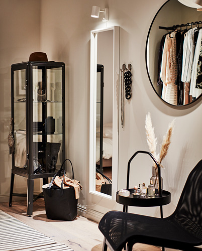 Dormitorio moderno con espejo LINDBYN negro con marco redondo y elegante que refleja un perchero y elementos de decoración.