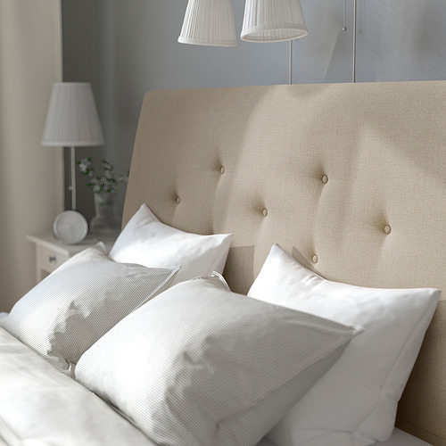 Cama beige con cabecero, cajones, almohadas blancas y lámpara.