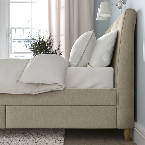 Elegante cama tapizada en color beige con cabecero inclinado, dos grandes almohadas blancas y una manta blanca doblada, que ofrecen comodidad y almacenamiento.