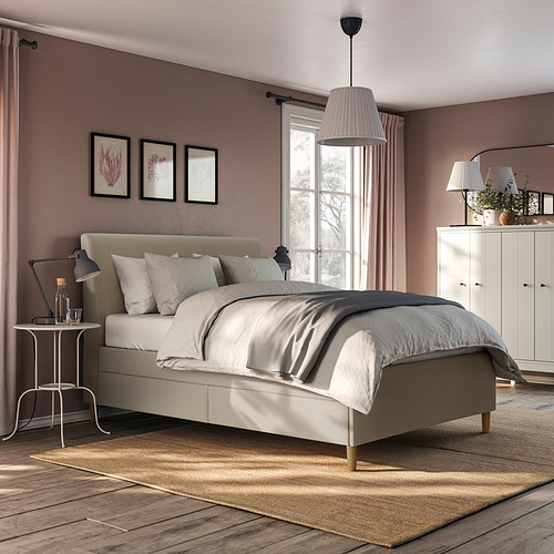Dormitorio moderno con cama beige IDANÄS, lámparas colgantes, cajones blancos y alfombra grande. La cama está centrada, los cajones a la derecha, la alfombra debajo.