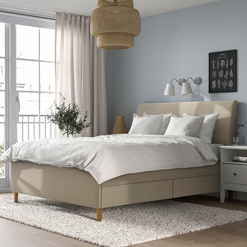 Dormitorio minimalista con cama beige, paredes azules, sábanas blancas y gran ventanal con cortinas transparentes. La lámpara colgante y la mesita de noche añaden una iluminación acogedora.