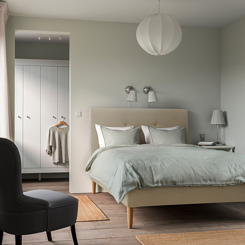 Dormitorio con cama IDANÄS, ropa de cama azul, lámpara colgante, silla negra sobre alfombra, armario blanco. Diseño tranquilo y minimalista.