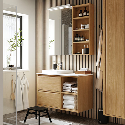 Baño moderno con mueble de madera marrón claro HAGAÅN, lavabo blanco y taburete negro.