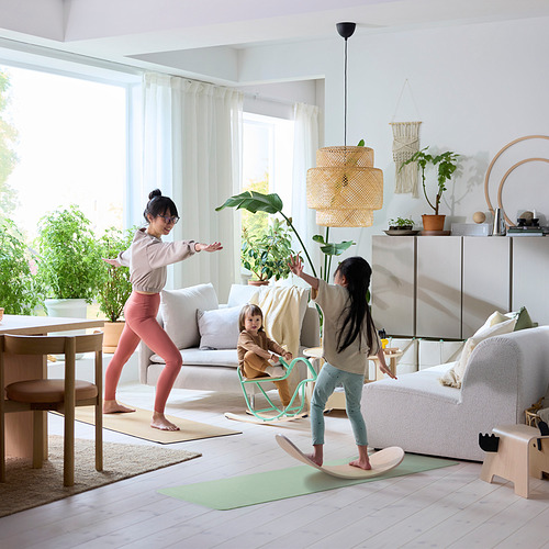 Niños jugando con tablas de equilibrio de madera en un salón luminoso con la madre estirándose cerca.