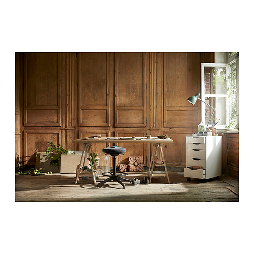 Configuración de oficina en casa con paredes de madera, un taburete de madera, una mesa y una cajonera blanca. La luz natural entra por una ventana.