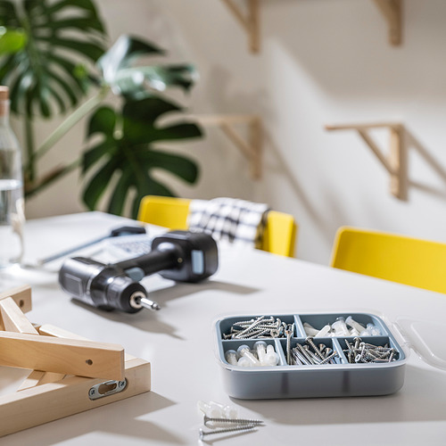 Caja de herramientas con pestillo con tornillos, taladro y planta sobre una mesa blanca.