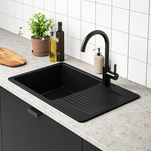 Fregadero de cocina moderno con grifo negro, bandeja y botellas en la encimera.