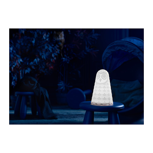 Lámpara blanca en forma de búho sobre taburete azul, da una suave luz ambiental.
