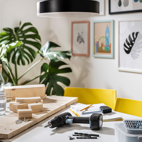 Espacio de trabajo bien iluminado con silla amarilla, planta, herramientas y obras de arte.