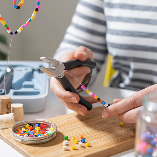 Las manos usan alicates TRIXIG para doblar el alambre con cuentas de colores. Herramientas y abalorios en tabla de madera para manualidades de bricolaje.