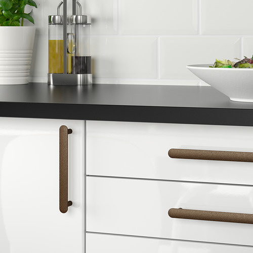 Cocina moderna con gabinetes blancos, manijas de bronce, encimera negra y ensalada.