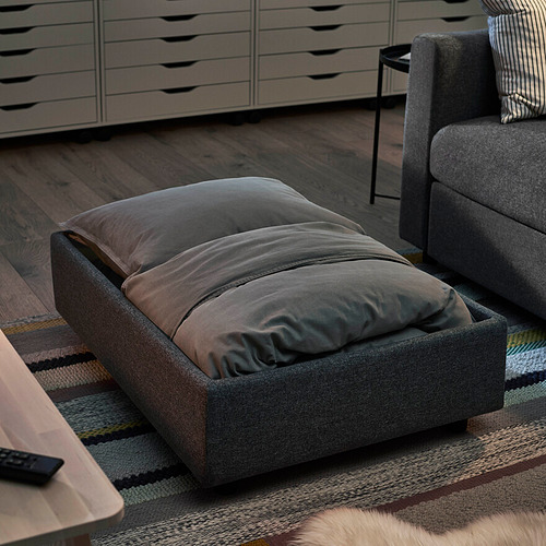 Reposapiés VIMLE gris sobre alfombra de rayas junto a sofá con suelo de madera.