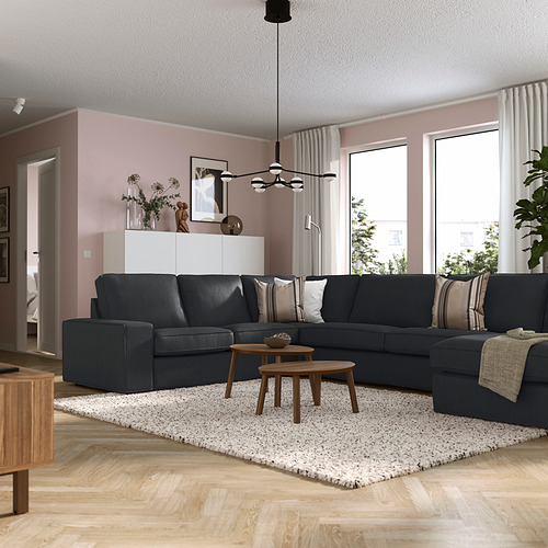 Salón moderno con sofá KIVIK, mesas de madera, paredes rosas, luz natural y lámpara colgante.
