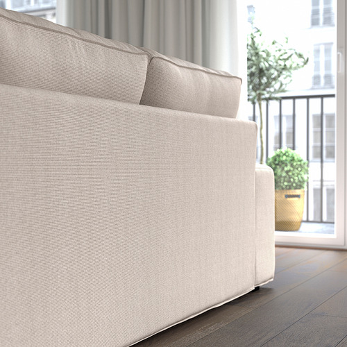 Un sofá KIVIK beige con reposabrazos bajos y muelles ensacados, que se muestra cerca de una ventana con plantas, que ofrece comodidad y apoyo para la relajación.
