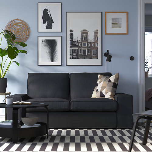 Sala de estar moderna con sofá gris KIVIK, alfombra en blanco y negro, arte de pared, plantas, lámpara y mesa de café.