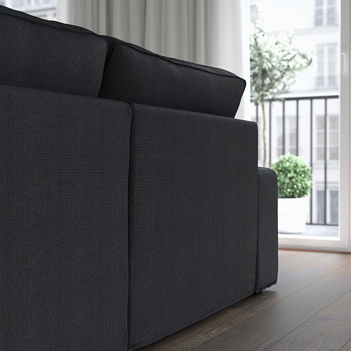 Sofá oscuro con reposabrazos bajos, colocado cerca de una ventana. Los amplios reposabrazos proporcionan soporte y zona de asiento adicional.