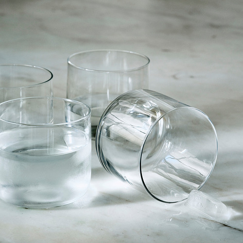 Tres tazas de vidrio soplado a boca sobre superficie ligera. Uno con un cubito de hielo cerca.