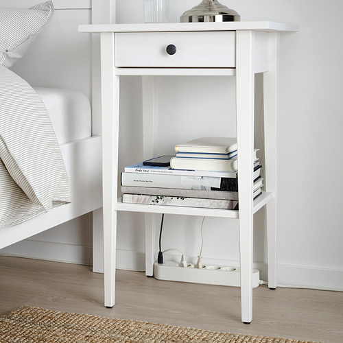 Mesita de noche blanca con cajón, libros, lámpara, usb, enchufes.