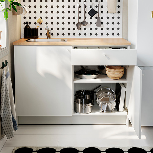 Cocina moderna con gabinetes blancos, encimera de roble y placa para salpicaduras de lunares. El cajón abierto revela sartenes, una canasta y ollas.