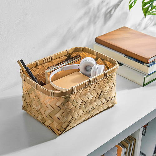Cesta de mimbre sobre el escritorio, con bolígrafos, cuadernos y auriculares. Conocido por su duradero bambú tejido a mano, es una solución de almacenamiento práctica y elegante.