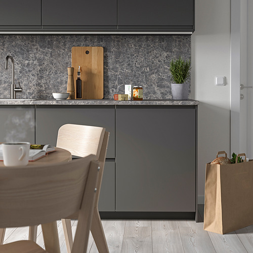Cocina pequeña, elegante y gris con gabinetes modernos, silla de madera y placa para salpicaduras de mármol. Una tabla de cortar, tazones y una planta pequeña se encuentran en el mostrador.