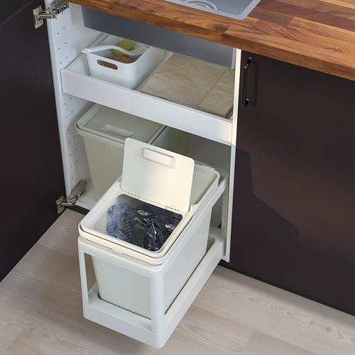 Un cubo de basura HÅLLBAR blanco debajo de un armario de cocina, con una tapa abierta llena de materiales reciclables, diseño innovador y práctico.