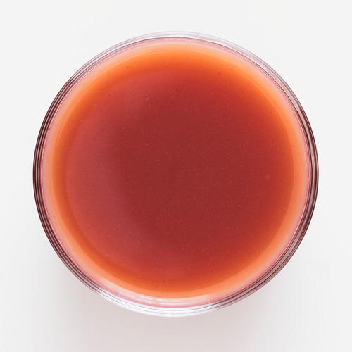 Un cuenco de vidrio transparente relleno de un batido espeso de frutos rojos con una textura brillante. Fresas frescas, frambuesas y arándanos destacados.