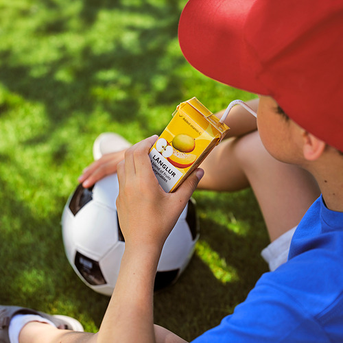 El niño bebe batido de lang lur amarillo, con pelota de fútbol, con gorra roja.
