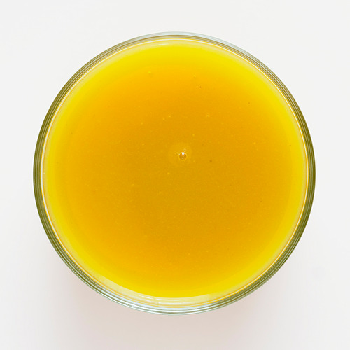 Un tazón de vidrio redondo y transparente lleno de un batido vibrante de color amarillo anaranjado hecho de mango, calabaza y manzana, que muestra una textura suave.