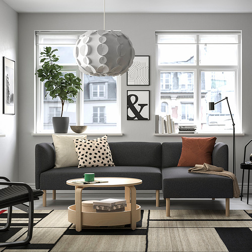 Sala de estar moderna con sofá modular LILLEHEM gris, cojines lumbares estampados, mesa de centro de madera, grandes ventanales y lámpara colgante.