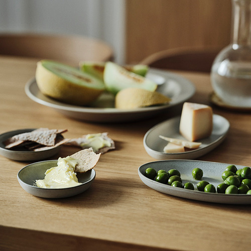 Platos pequeños con pan, queso, guisantes y salsa en una mesa de madera.