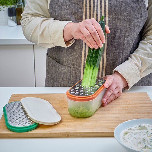 Una persona ralla un pepino directamente en un recipiente de UPPFYLLD sobre una tabla de cortar de madera.