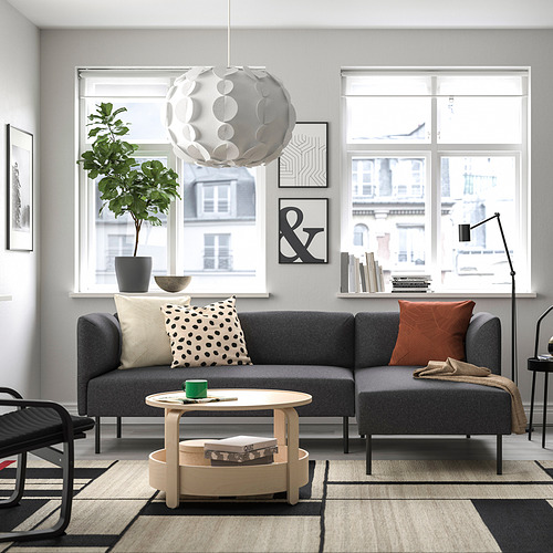 Salón moderno: sofá modular LILLEHEM gris con detalles en madera, elegante lámpara colgante, alfombra estampada y grandes ventanales con vistas urbanas.