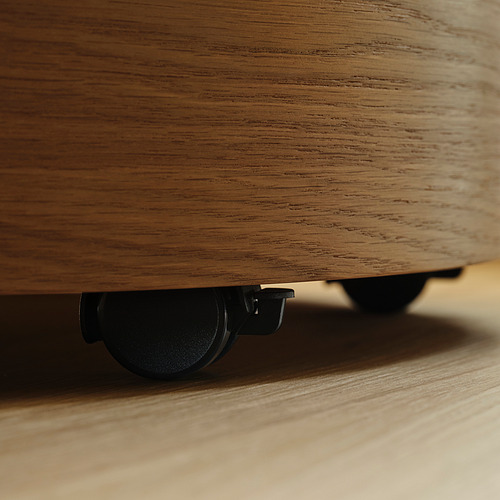 Primer plano de la parte inferior de un mueble de madera clara, que muestra una rueda giratoria oculta para facilitar el movimiento.