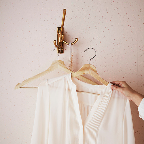 Una percha de madera sujeta una blusa blanca en un gancho de latón, mostrando su diseño antideslizante con ranuras.