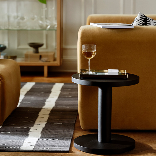 Una pequeña mesa redonda negra sostiene una copa de vino, junto a una gran silla beige, sobre una alfombra gris a rayas.