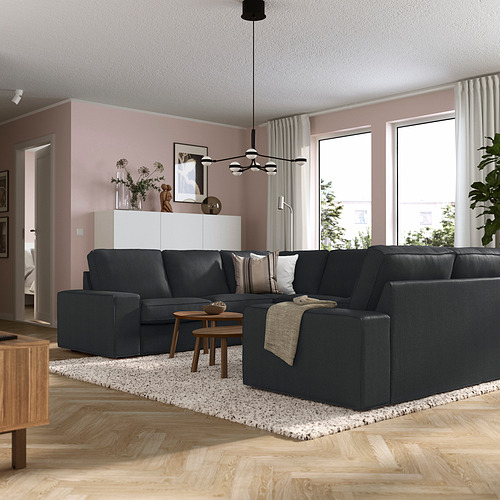Sala de estar moderna con un gran sofá KIVIK gris, mesa de centro de madera y paredes rosas. El sofá es grande y se adapta cómodamente a varias personas.