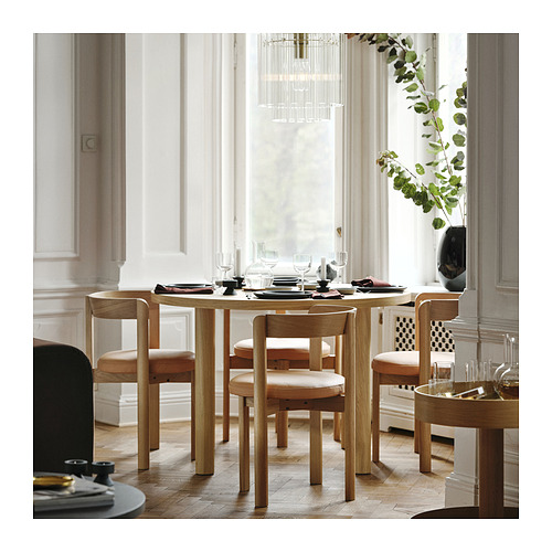 Comedor moderno con mesa de roble, sillas, cristalería, platos, lámpara de araña y una gran ventana.