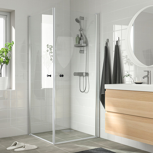 Baño moderno y minimalista con ducha de vidrio de dos puertas, tocador elegante, espejo redondo y toallas oscuras.
